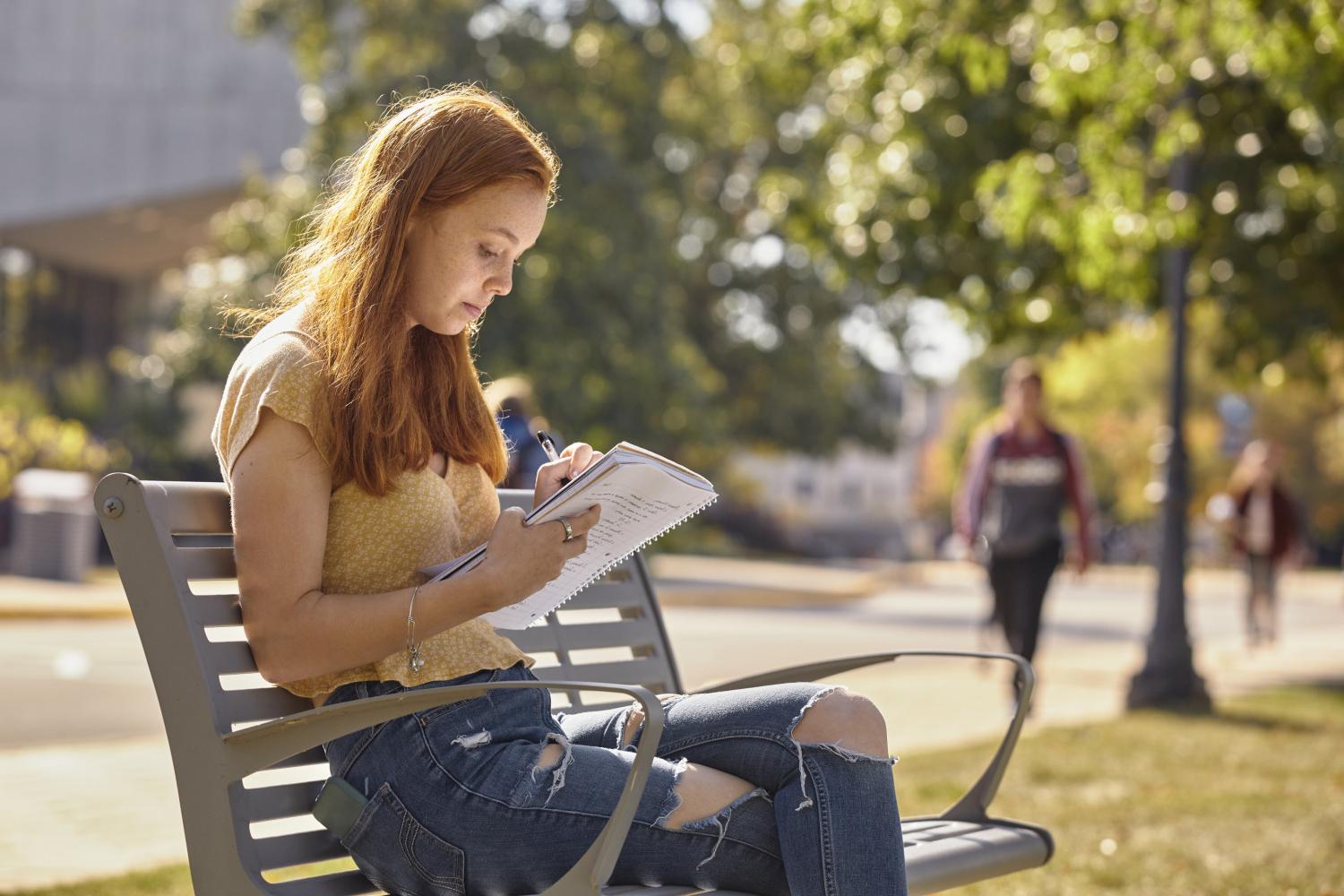 A <a href='http://65bv.mokmingsky.com'>全球十大赌钱排行app</a> student reads on a bench along Campus Drive.